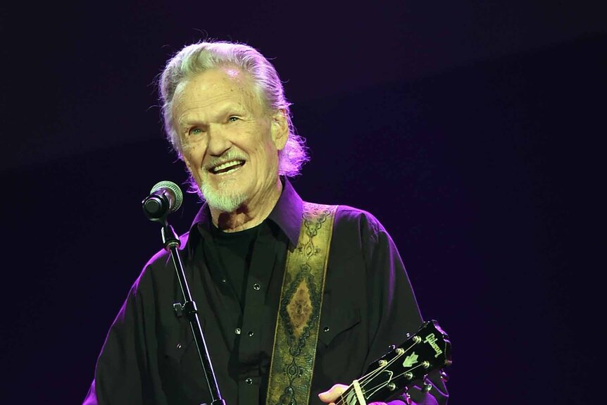 Kris Kristofferson smiles while performing with a guitar.