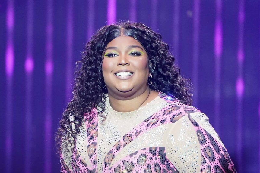Lizzo smiles in front of a purple backdrop.