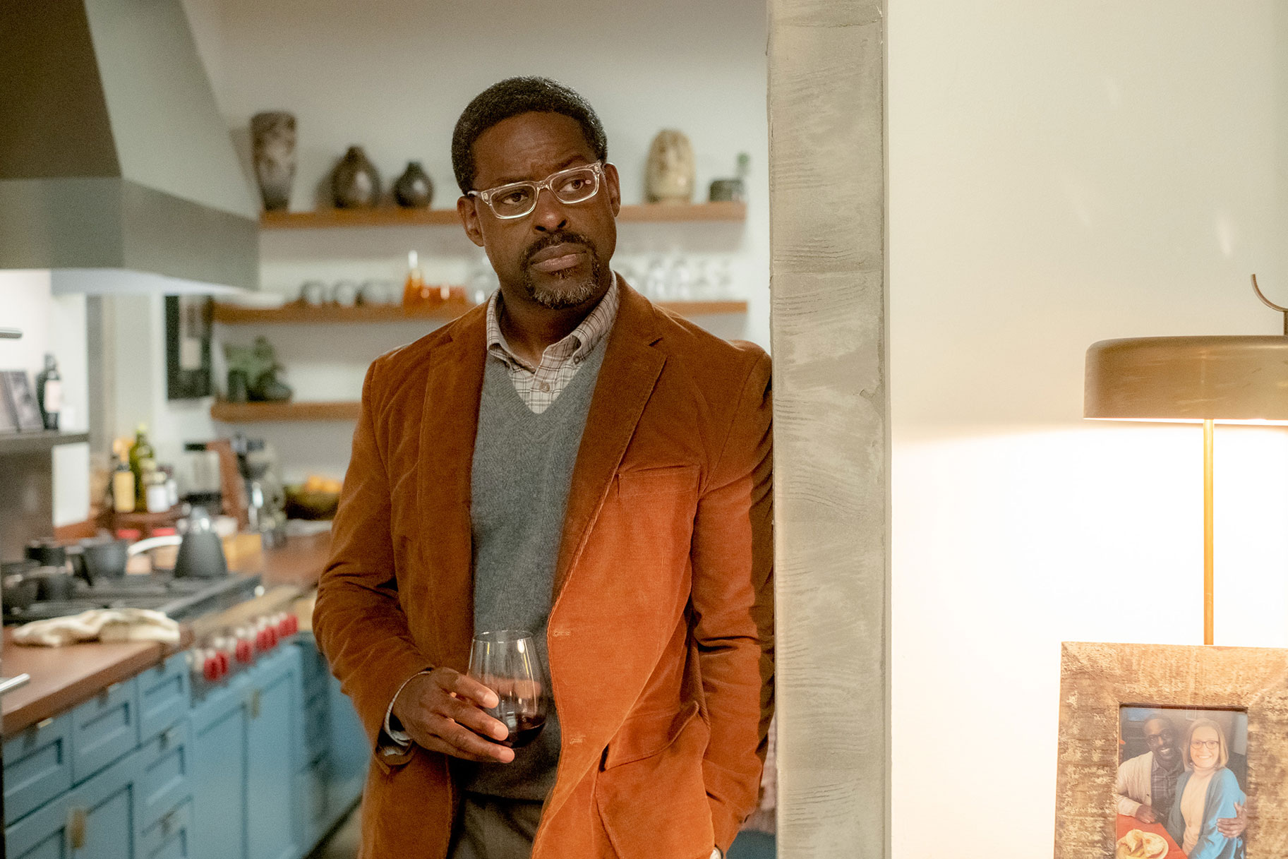 Randall leaning against a doorway with a cup in his hand