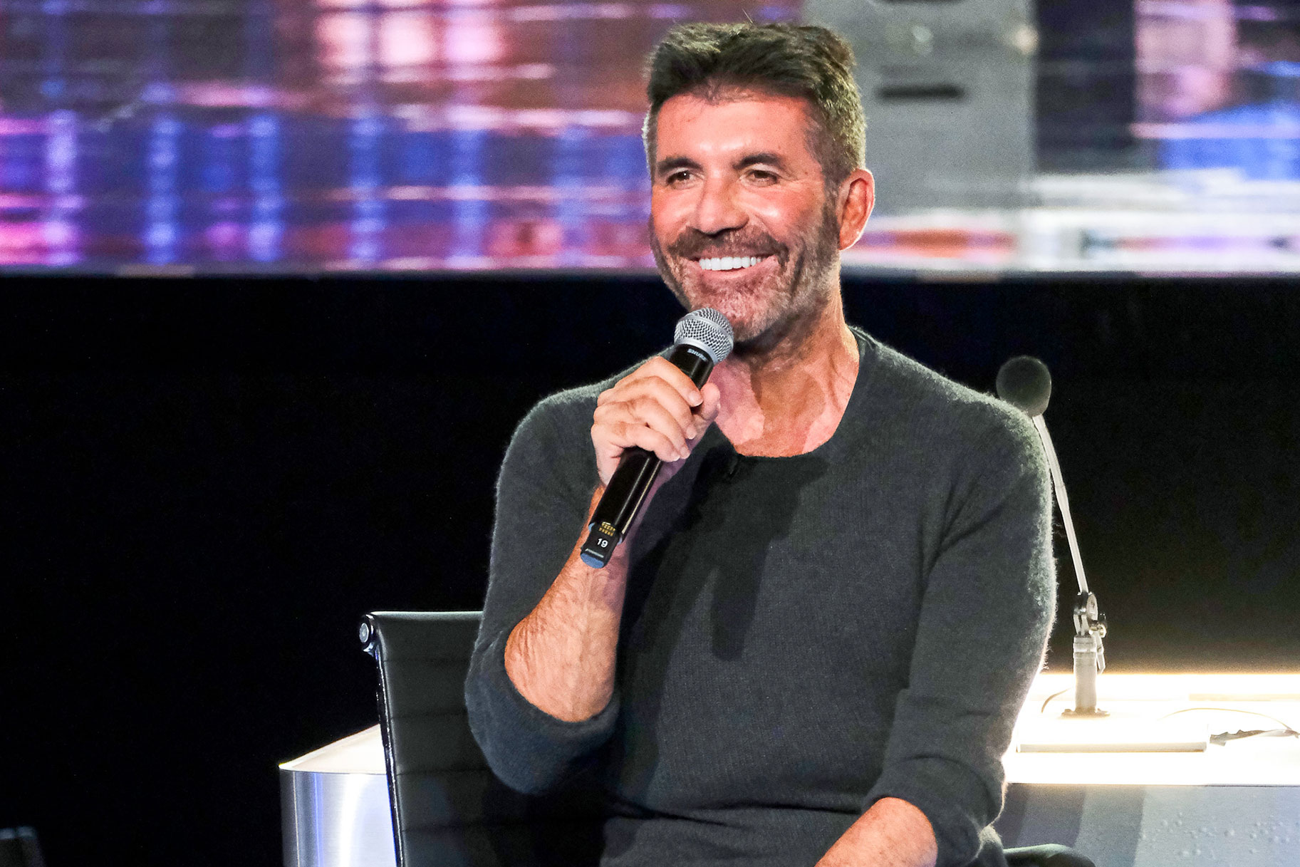 Simon Cowell smiling while holding a mic up to his lips