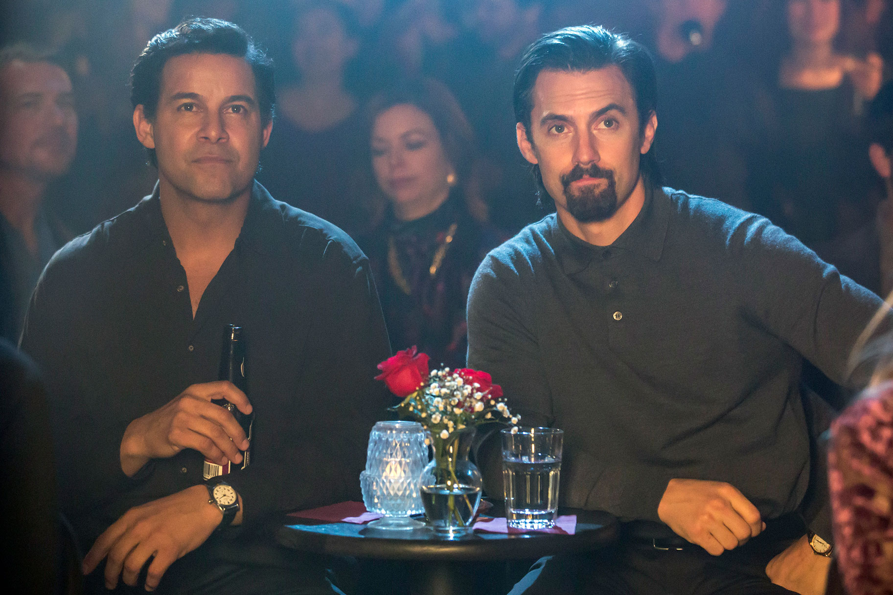 Jack and Miguel looking offscreen while sitting in a dark room at a small table