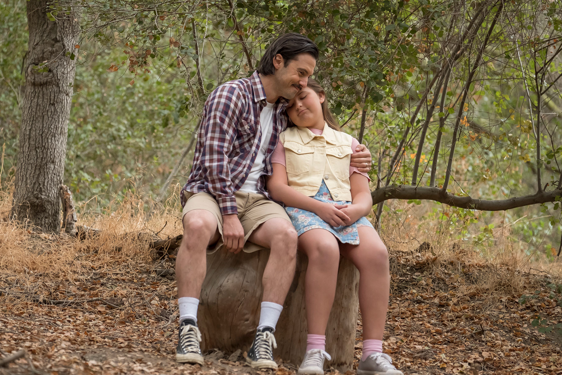 Jack and young kate embrace while sitting on a tree stump in the woods