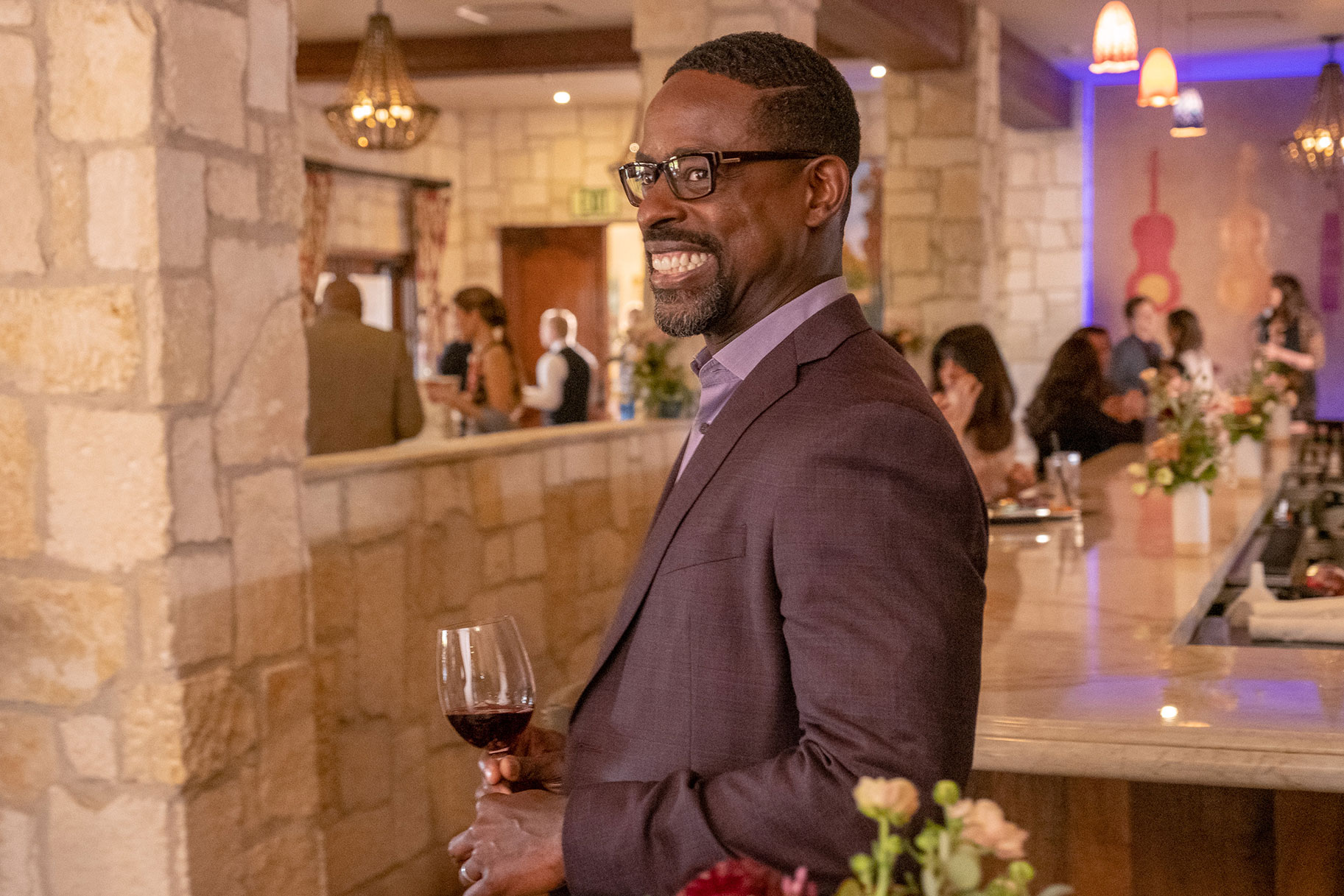 Randall smiling while holding a glass of red wine during Kate's wedding