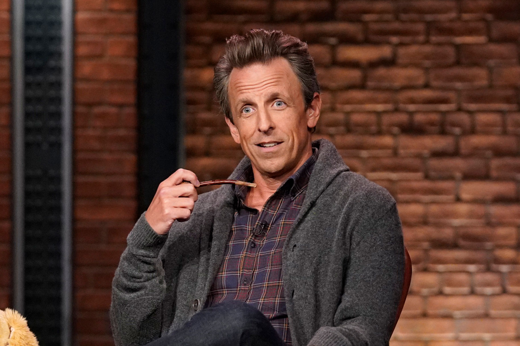 Seth Meyers sitting in a chair, smoking a pipe