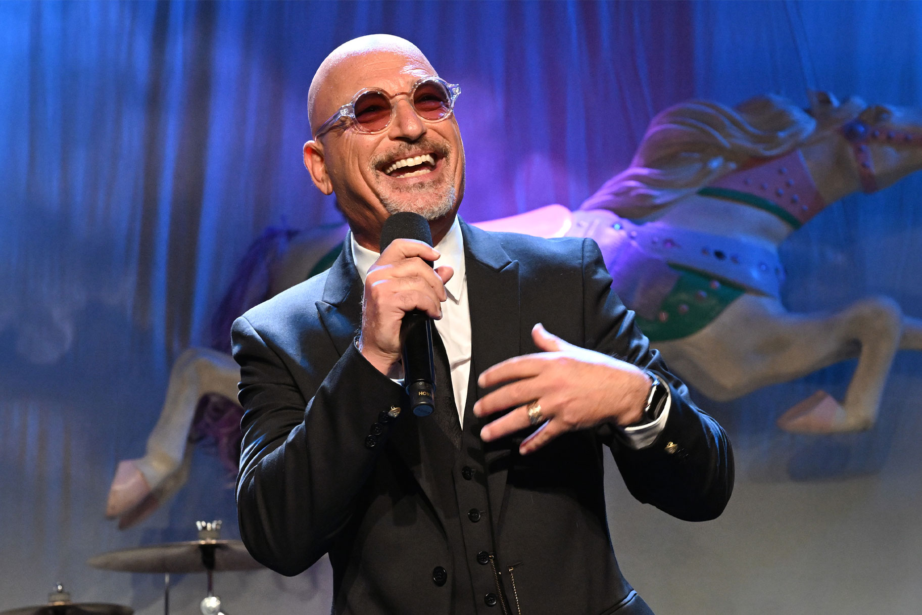 Howie Mandel smiling and speaking into a mic onstage