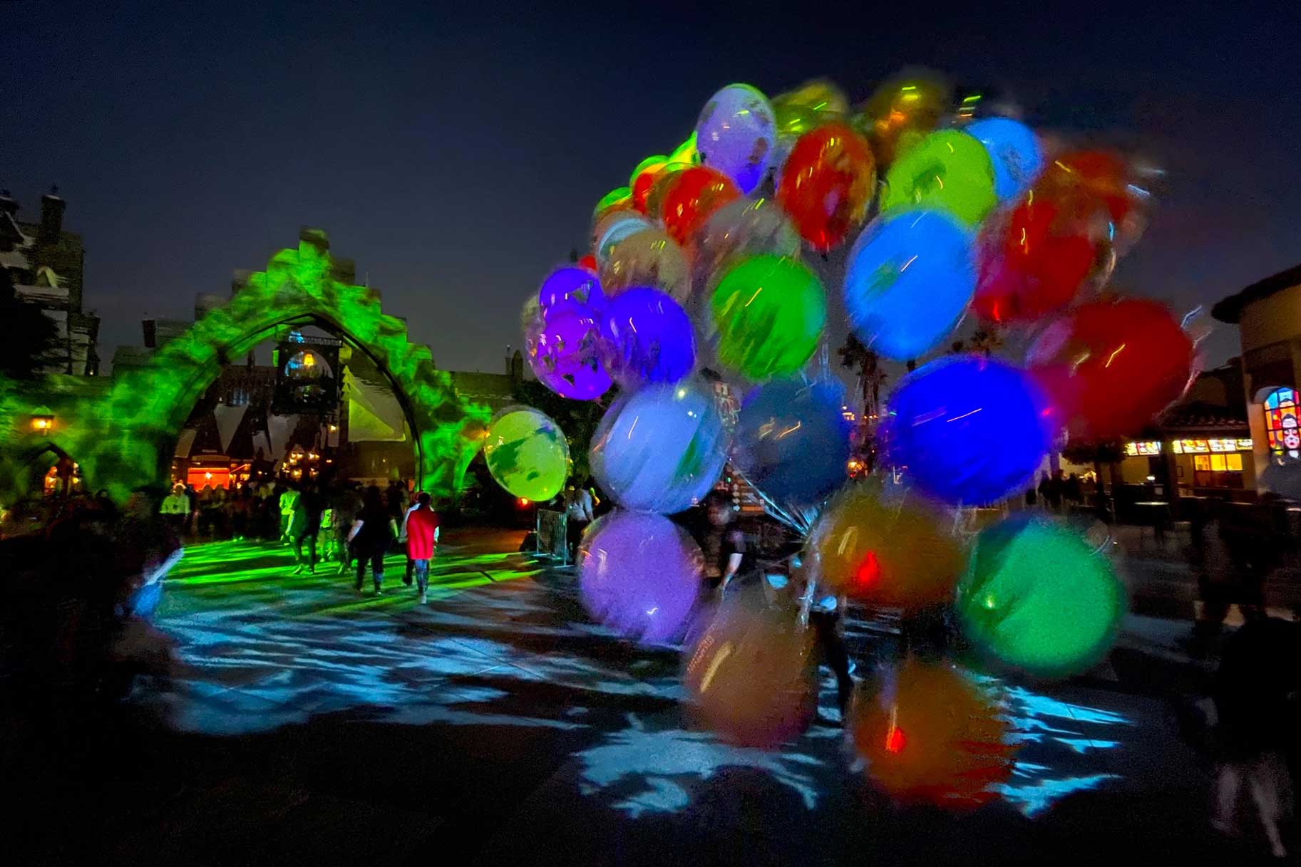 Guests walking down a dark pathway that's lit up green with balloons in the view.