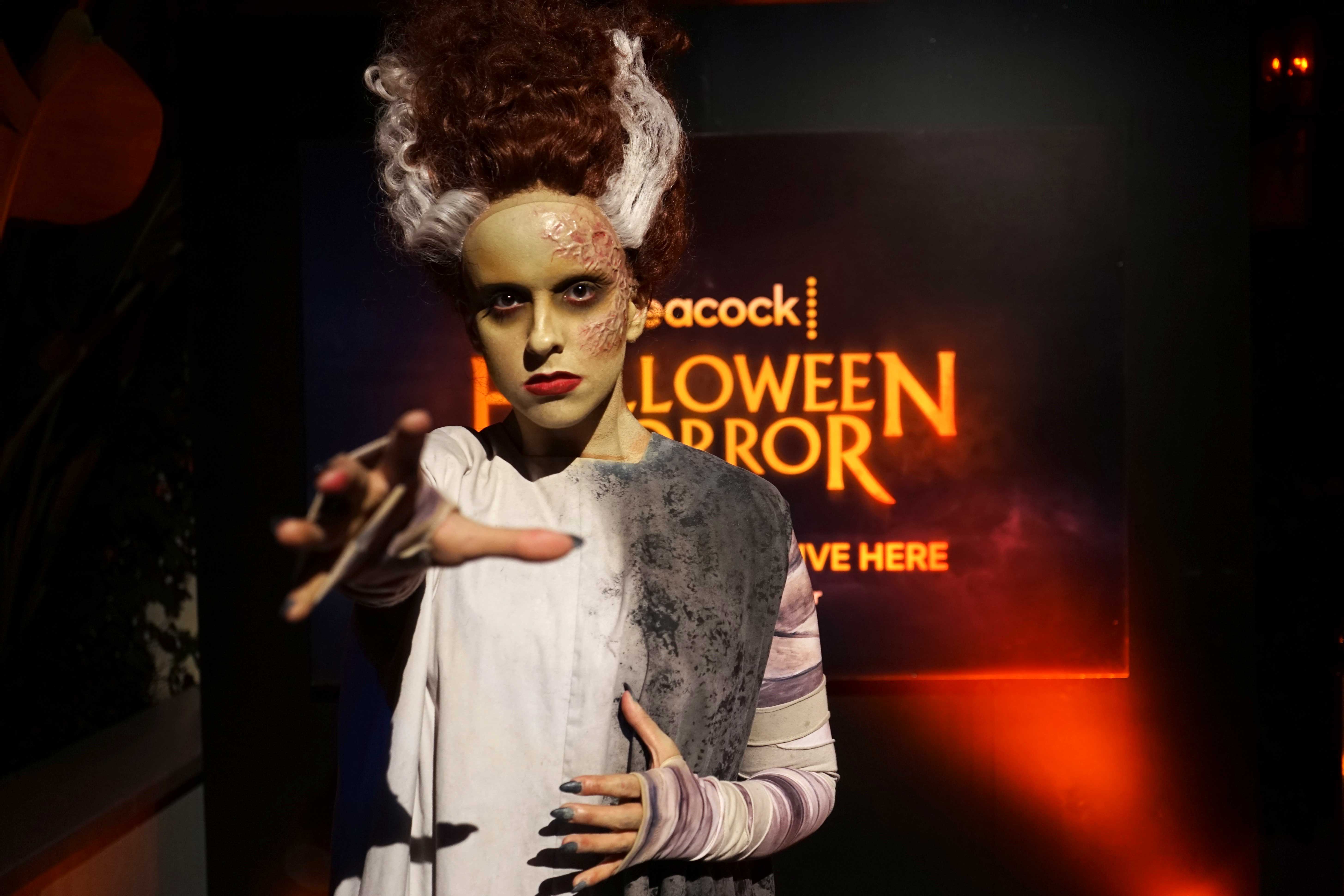 A scare actor dressed as the Bride of Frankenstein with their hand stretched out to the camera.