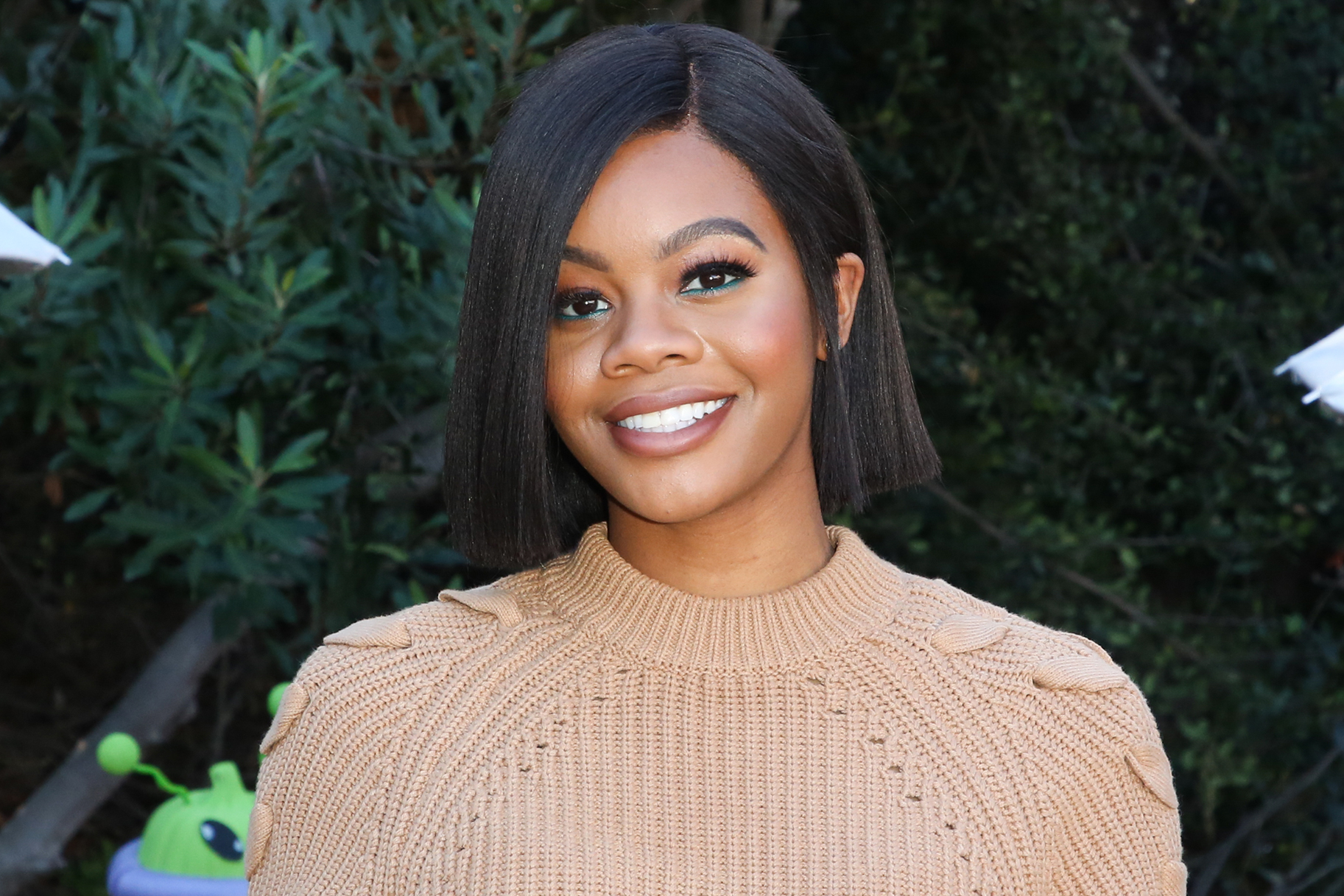 Gabby Douglas smiles in a tan sweater during Hallmark's "Home & Family" event