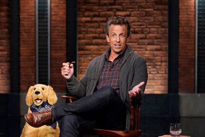 Seth Meyers sitting in a chair on the set of 'Late Night'