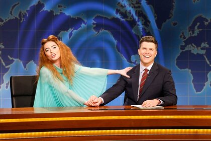 Sarah Sherman dressed as Genesis Fry putting her hand on Colin Jost while laughing during The Weekend Update.