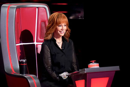 Reba McEntire sits smiling in her coach's chair