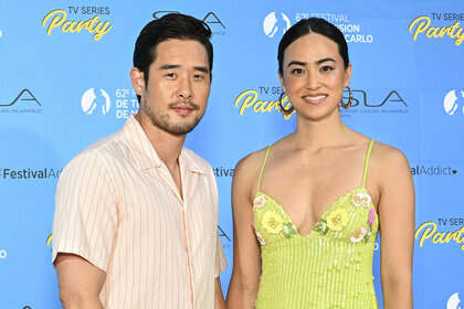 Raymond Lee stands in front of a step and repeat with his wife Stacy Kusumolku
