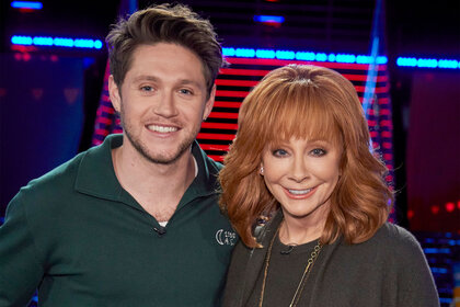 Niall Horan and Reba McEntire smile and pose for the camera on the set of The Voice