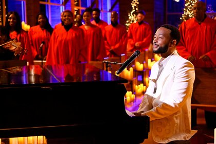 John Legend singing and playing piano while a choir is singing in the background.