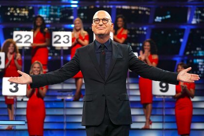 Howie Mandel posing with his arms out with the Briefcase Models wearing red dresses in the background.