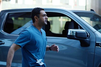 Dr. Bashir Hamed wearing blue scrubs outside while running next to a blue car.