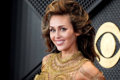 Miley Cyrus smiles in a gold outfit.