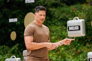 Joe Manganiello speaks with briefcases and dollar amounts suspended behind him in Deal or No Deal Island Episode 102