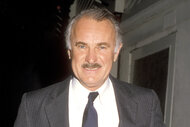Dabney Coleman smiles in a grey suit and tie