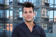 Dez Duron leans on a fence in front of a building