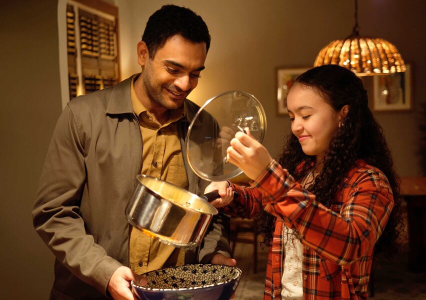Amira Hamed holding a pot and a lid showing a dish to Dr. Bashir Hamed.