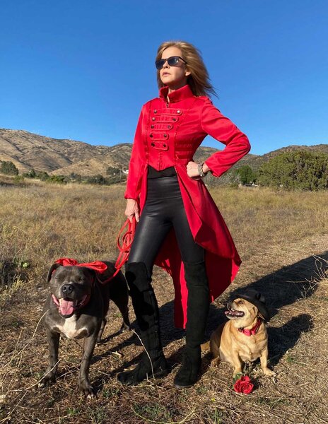 Linda Blair posing outside wearing a red top. She is standing next to two dogs.