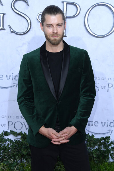 Luke Mitchell standing in front of a step and repeat in a green velvet suit.