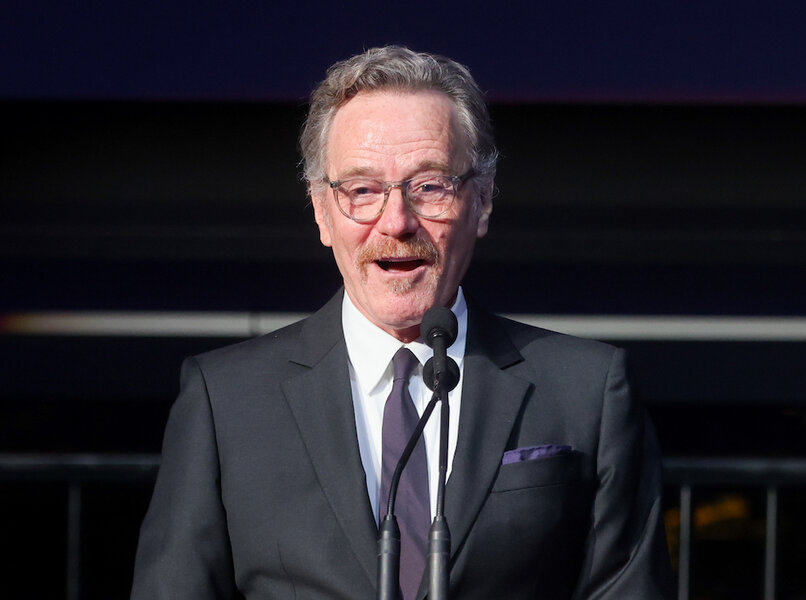 Bryan Cranston wears glasses and speaks at a podium.
