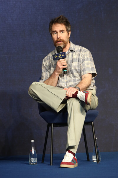 Sam Rockwell sits onstage and speaks into a microphone.