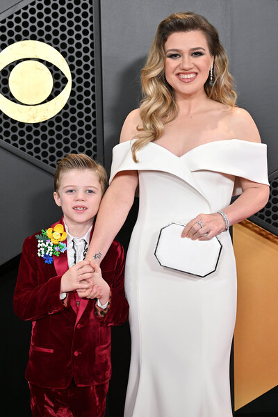 Kelly Clarkson smiles holding her sons hand on the red carpet of the 2024 Grammys