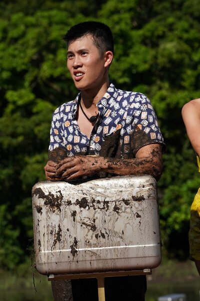 Brantzen Wong leans on a muddy briefcase in Deal or No Deal Episode 101.
