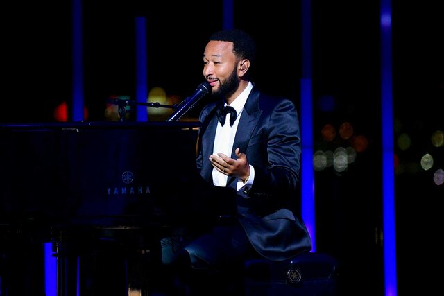 John Legend playing piano and singing on stage.