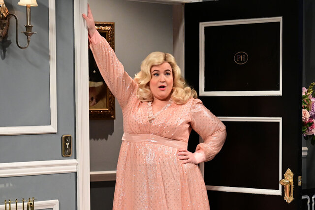 Aidy Bryant leans against a doorframe while wearing long sleeve light pink dress during the "Aidys Dream" SNL sketch