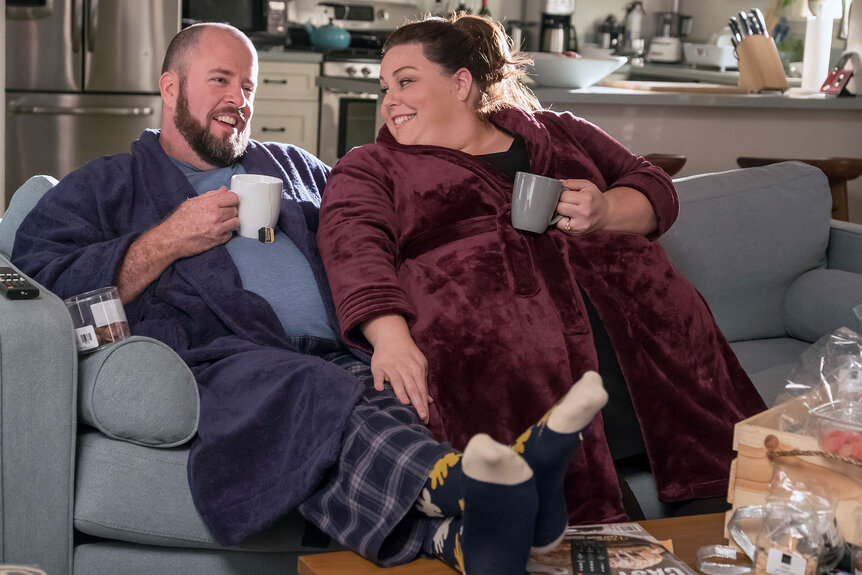 Kate And Toby dressed in their robes, sitting on their couch drinking tea together