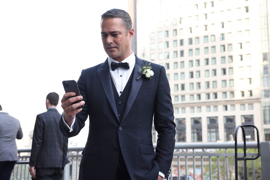 Kelly Severide checking his phone while wearing a black tuxedo