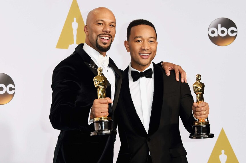 Common and John Legend posing in the Grammy's press room holding their awards.