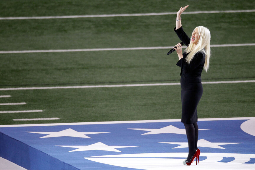 Christina Aguilera stands in the middle of a football field while singing the national anthem