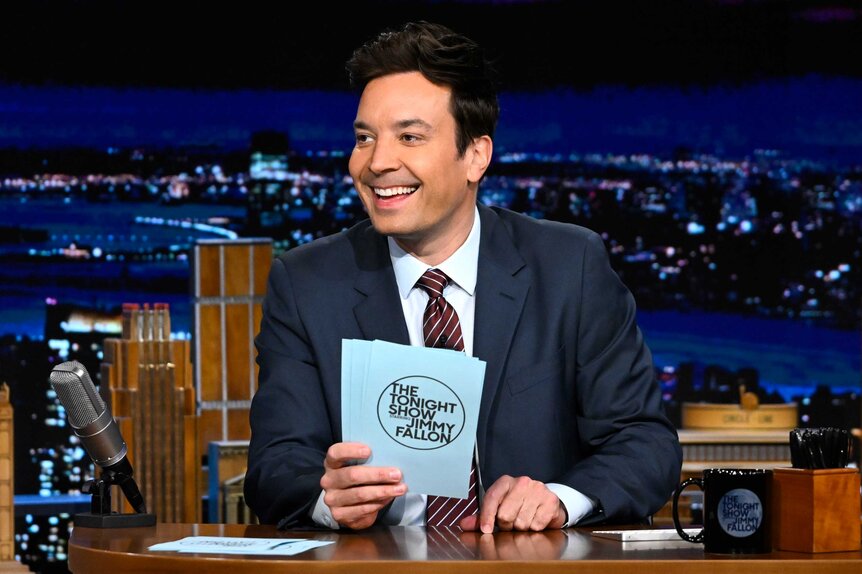 Jimmy Fallon sitting at his desk during The Tonight Show.