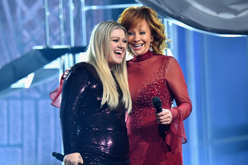 Kelly Clarkson and Reba McEntire hugging on stage.