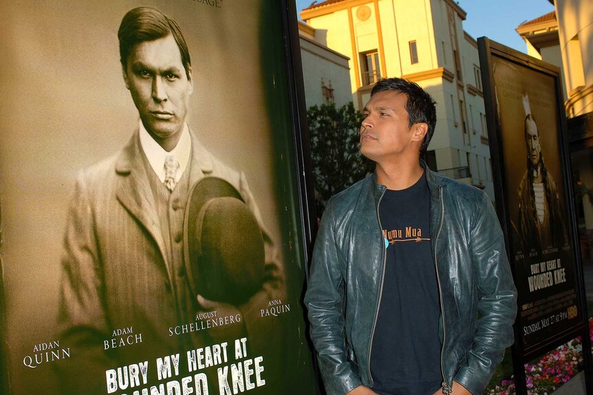 Adam Beach poses with the movie poster for Bury My Heart At Wounded Knee.