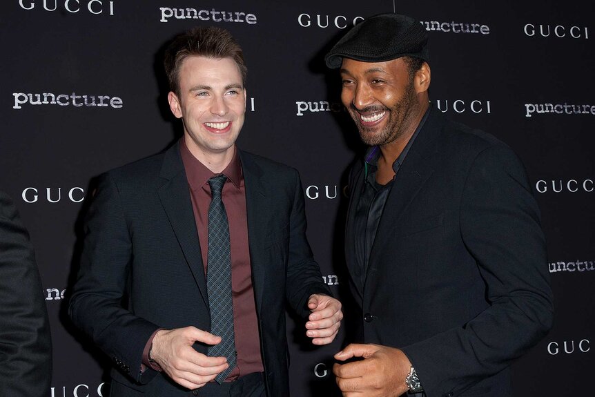 Chris Evans and Jesse L. Martin dressed in black suits, smiling and posing for photos at the Puncture premiere in 2011.