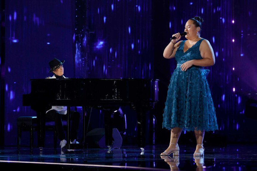 Diane Warren playing piano while Lavender Darcangelo sings on stage.