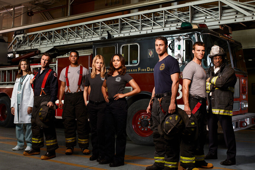 The cast of Chicago Fire from the pilot episode pose in front of a fire truck