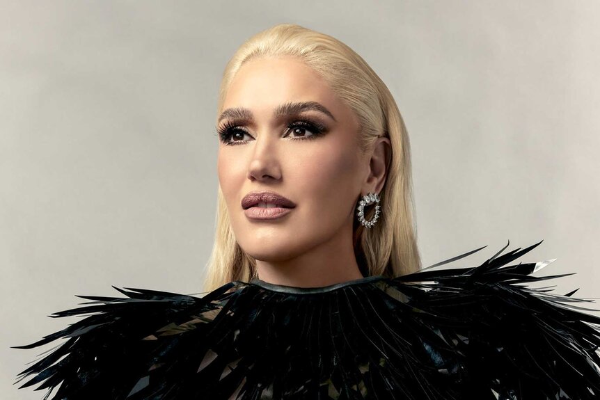 Gwen Stefani, wearing a black feather top, looking off into the distance while posing for the camera.