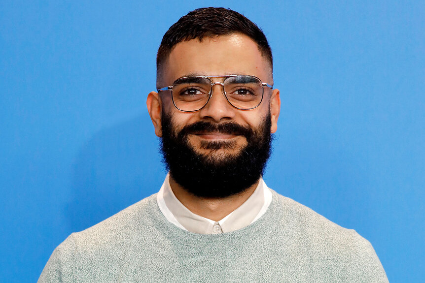 Hamza Haq smiling in front of a bluebackground