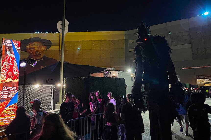 Guests waiting in line next to a tall demon scare actor.