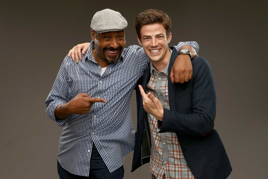 Jesse L. Martin and Grant Gustin posing for a portrait in front of a gray backdrop.