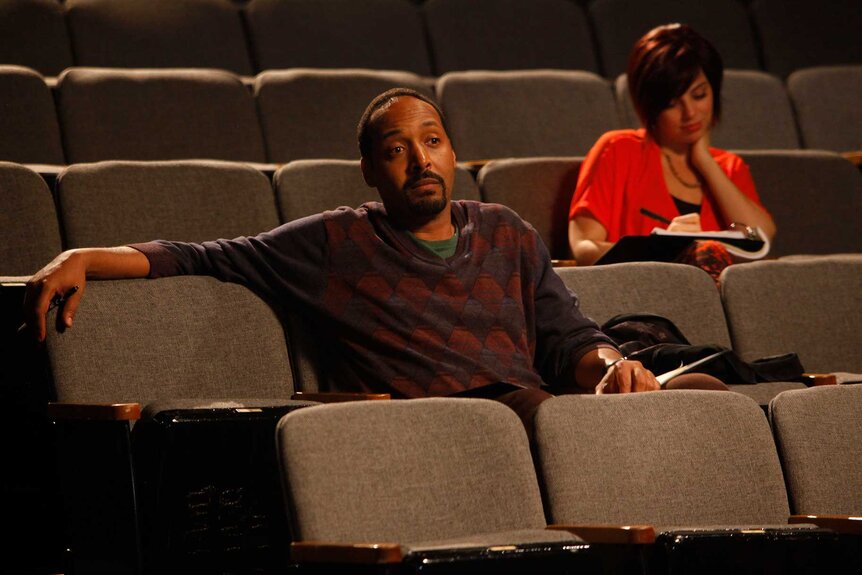 Scott sitting in a theater with his arm over a chair looking at the stage.