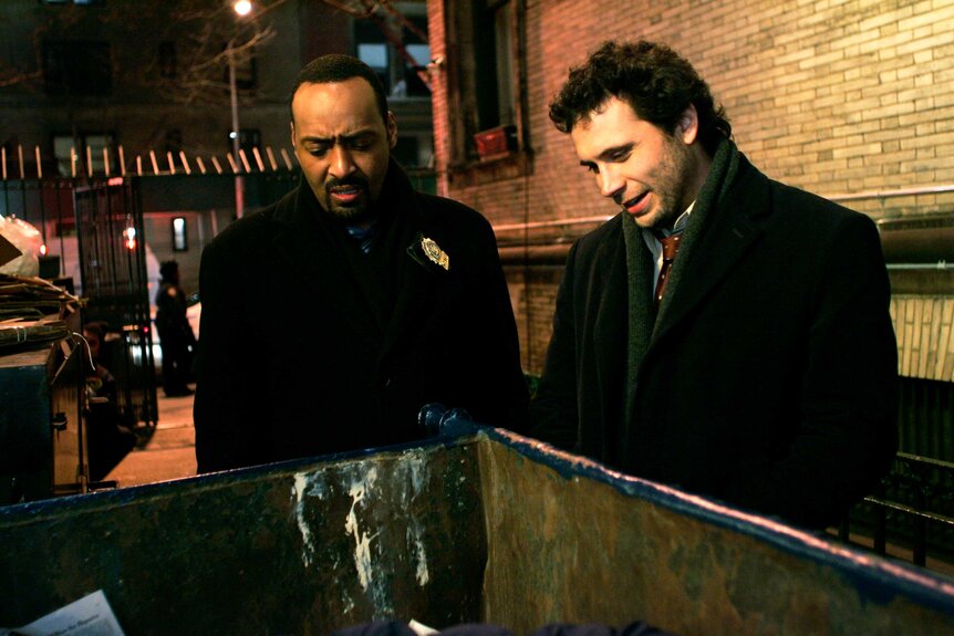 Detective Ed Green and Detective Cyrus Lupo looking in a trash can during an episode of Law & Order.