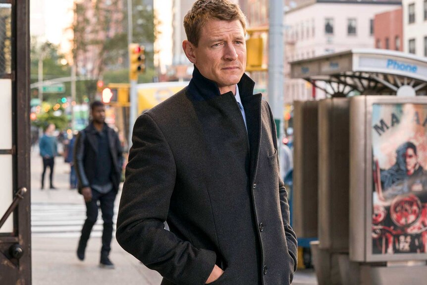 Peter Stone in a black trench coat looking off into the distance.